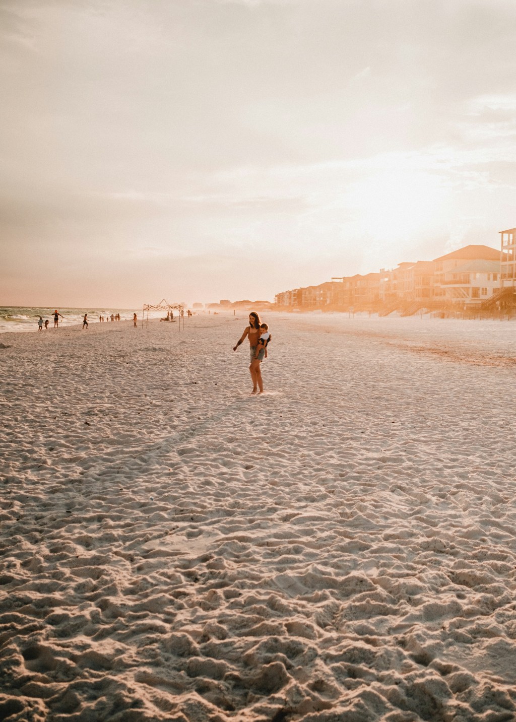 A tired mom walking on the beach holding hands with her children, the sun low on the horizon, symbolizing quiet strength and moments of connection amid chaos.